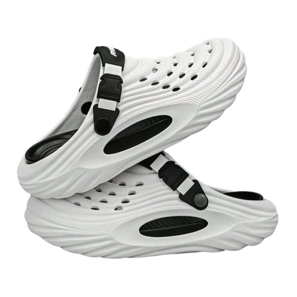 Overhead stylized shot of a person’s feet in white Piki closed-toe clogs, standing on a light wooden floor, paired with navy blue medical scrubs or white chef trousers.