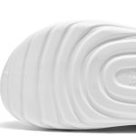 Overhead stylized shot of a person’s feet in white Piki closed-toe clogs, standing on a light wooden floor, paired with navy blue medical scrubs or white chef trousers.