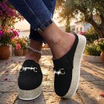 Close-up lifestyle shot of women's black canvas platform mule espadrilles with a chunky jute rope sole and a sparkling gold chain buckle, worn with distressed jeans and a silver anklet.