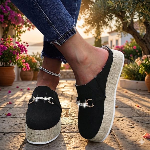 Close-up lifestyle shot of women's black canvas platform mule espadrilles with a chunky jute rope sole and a sparkling gold chain buckle, worn with distressed jeans and a silver anklet.