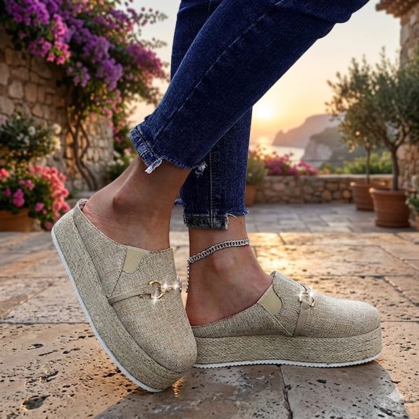 Professional lifestyle shot of Piki Comfort platform mule espadrilles in natural tan linen with a sparkling gold chain accent, worn by a model on a Mediterranean terrace during a golden hour sunset.