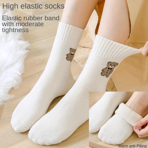 Hand holding white ribbed crew socks with cat embroidery.