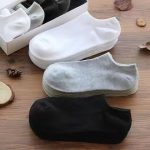 A selection of white, grey, and black Men's Short Socks laid out on a wooden surface with a storage box.