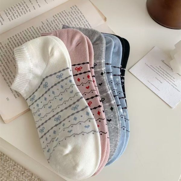 A fanned-out bundle of five pairs of ankle socks with dainty bow and heart patterns, laid next to a book.