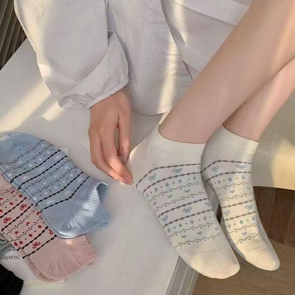 A person wearing white Sweetheart Bow ankle socks with a preppy aesthetic, with other socks from the bundle nearby.