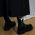 A person wearing black Whimsical Crew socks with a flower design paired with black Mary Jane shoes.
