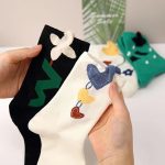 Close-up of hands holding two pairs of Whimsical Crew socks with cartoon floral and heart designs.